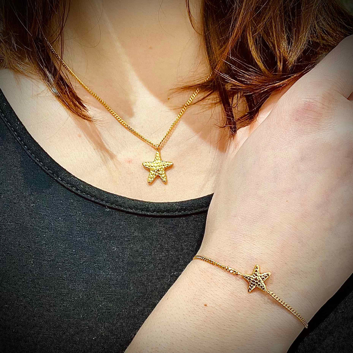 Kette und Armband mit Seestern in Gold, getragen von einer Frau im schwarzen Shirt