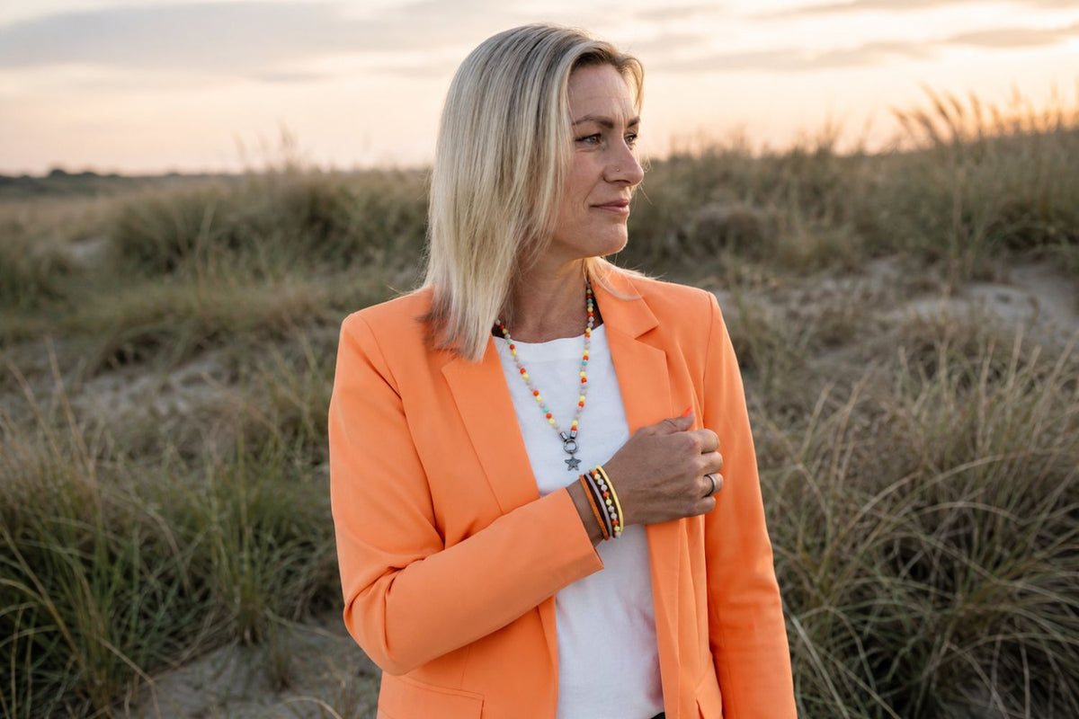 Blonde Frau im orangefarbenen Blazer in den Dünen im Abendlicht