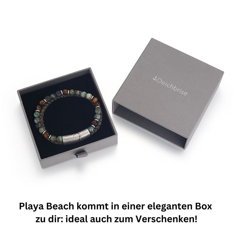 The Armband Playa Beach (Multistrang) with taupe leather, African turquoise, and tiger eye beads is displayed in an open grey Deichbrise gift box featuring German text below. The box highlights the bracelet’s distinctive style.