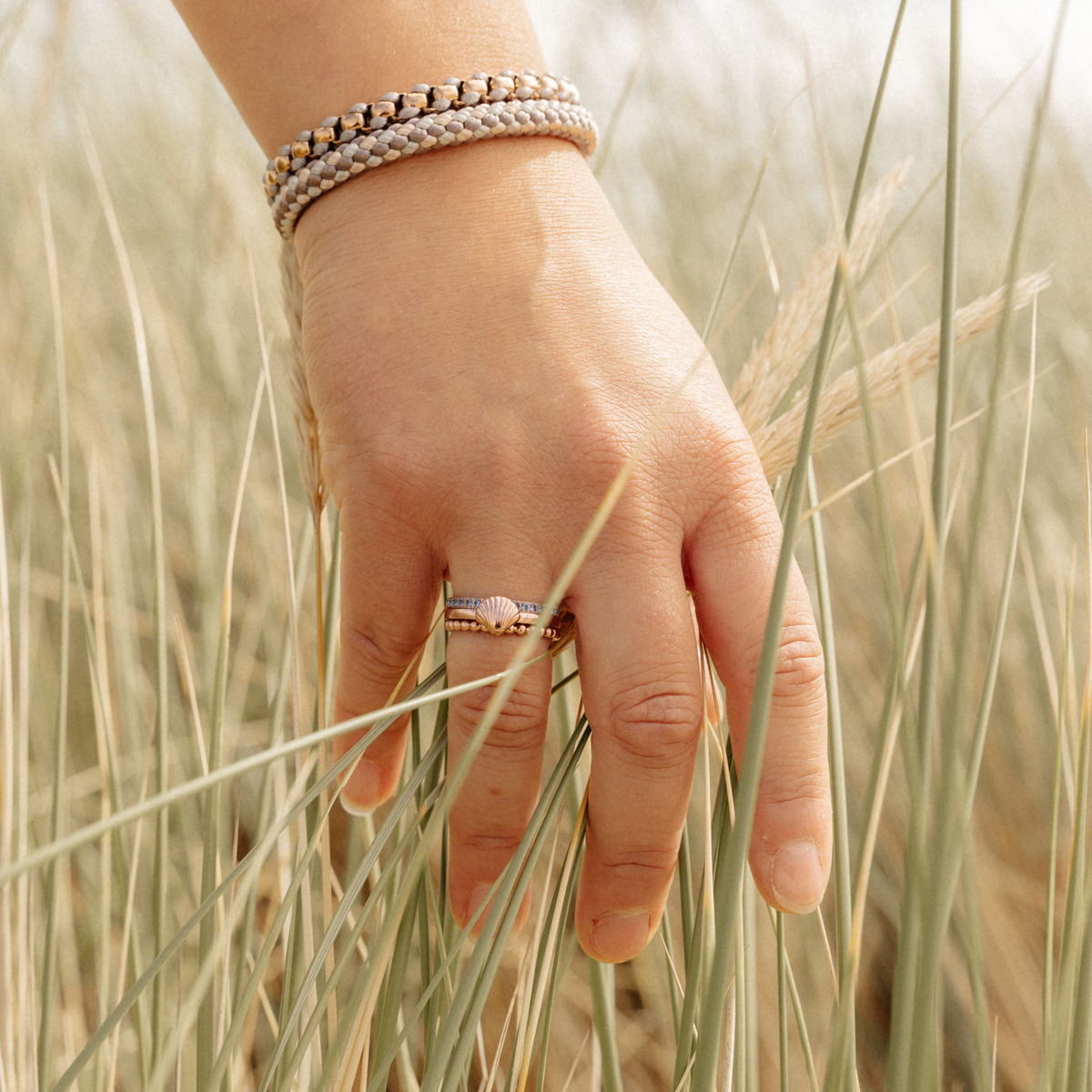 Hand im Dünengras mit dem Ring Bling Bling mit blauen Steinen, dazu Armbänder